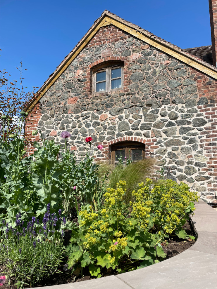 Großer Garten im Sommer, hinter dem Haus mit Blumenbeet und Natursteinplatten in Sonstige
