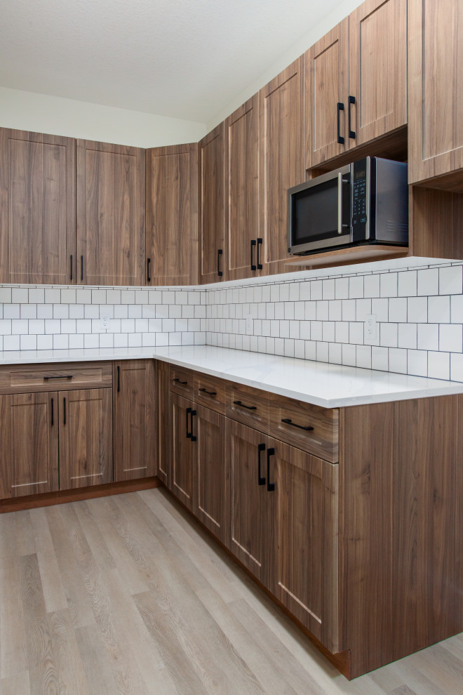 Mid-sized country l-shaped kitchen pantry in Edmonton with quartz benchtops, white splashback, ceramic splashback, beige floor, white benchtop, an undermount sink, shaker cabinets, medium wood cabinets, stainless steel appliances, vinyl floors and with island.