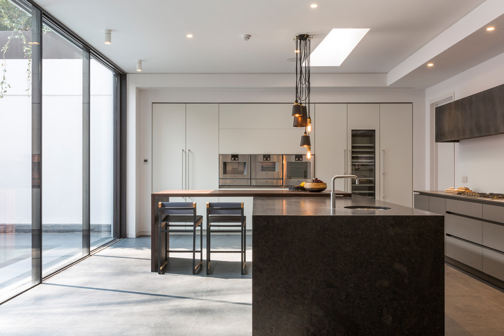 This is an example of a large contemporary l-shaped kitchen in London with an undermount sink, flat-panel cabinets, grey cabinets, stainless steel appliances, with island, grey floor and black benchtop.