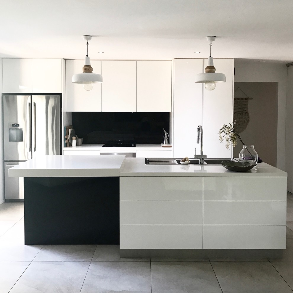 Design ideas for a mid-sized contemporary single-wall eat-in kitchen in Other with a drop-in sink, flat-panel cabinets, white cabinets, limestone benchtops, black splashback, ceramic splashback, stainless steel appliances, cement tiles, with island and grey floor.