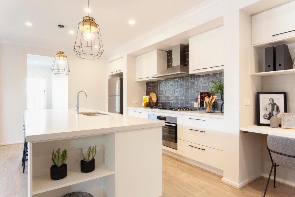 This is an example of an industrial kitchen in Melbourne with an undermount sink, white cabinets, quartz benchtops, grey splashback, ceramic splashback, stainless steel appliances, laminate floors, with island, beige floor and white benchtop.