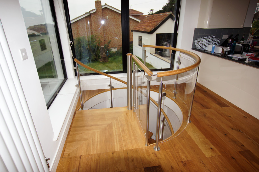 Imagen de escalera de caracol moderna de tamaño medio con escalones de madera, contrahuellas de vidrio y barandilla de vidrio
