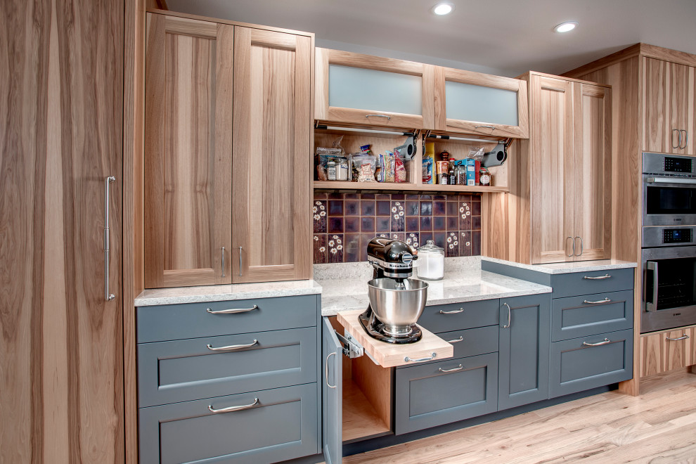 Photo of a large eclectic u-shaped open plan kitchen in Seattle with a belfast sink, flat-panel cabinets, blue cabinets, engineered stone countertops, multi-coloured splashback, ceramic splashback, stainless steel appliances, light hardwood flooring, a breakfast bar, brown floors and grey worktops.