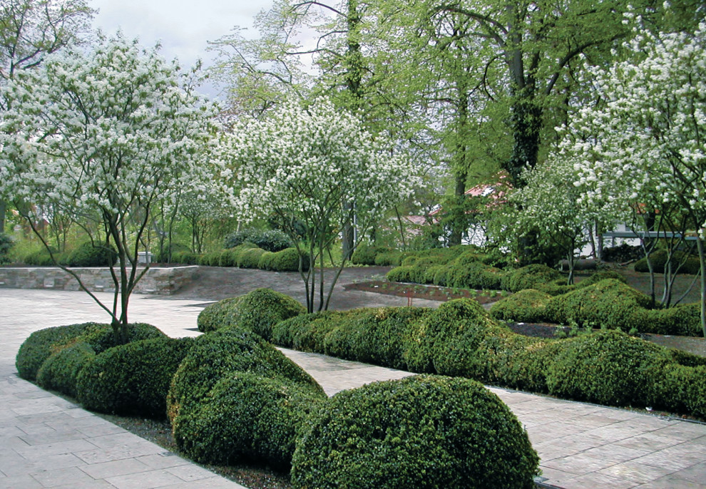Aménagement d'un grand jardin avant classique avec un massif de fleurs, des pavés en pierre naturelle et une clôture en métal.