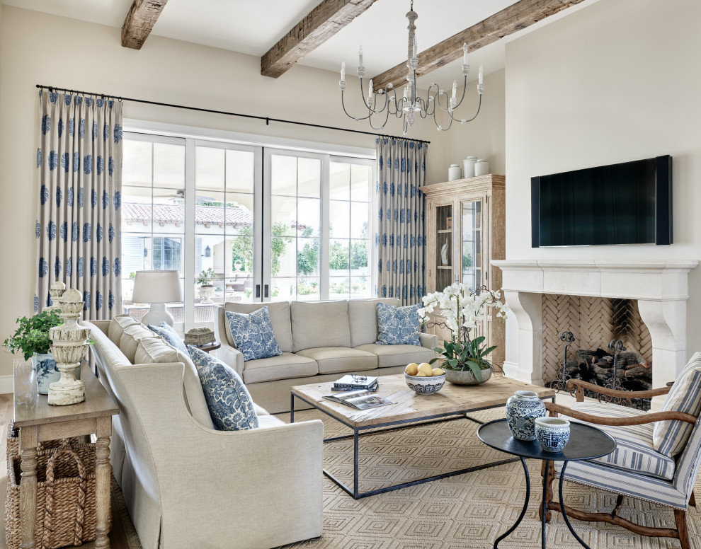 This is an example of a large mediterranean open concept living room in Phoenix with beige walls, medium hardwood floors, a standard fireplace, a plaster fireplace surround, a wall-mounted tv and beige floor.