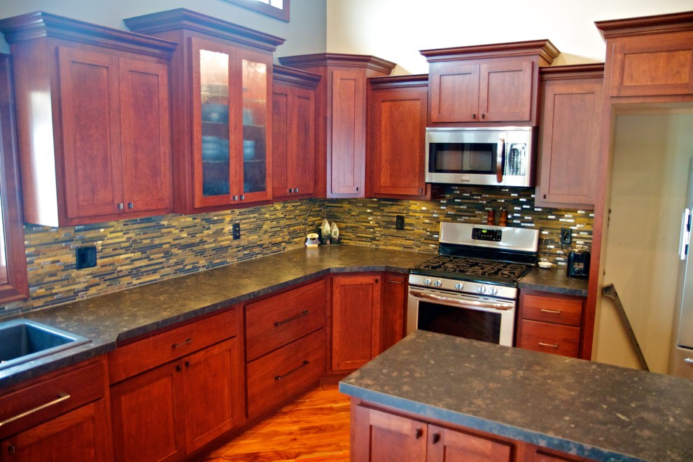 Example of a large l-shaped light wood floor open concept kitchen design with a drop-in sink, shaker cabinets, dark wood cabinets, laminate countertops, multicolored backsplash, stone tile backsplash, stainless steel appliances and an island