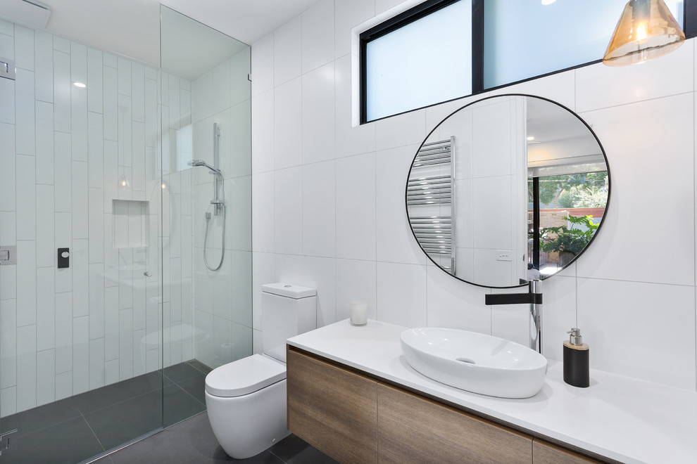 Photo of a mid-sized contemporary 3/4 bathroom in Melbourne with flat-panel cabinets, medium wood cabinets, a curbless shower, a two-piece toilet, white tile, white walls, a wall-mount sink, grey floor, a hinged shower door, white benchtops and granite benchtops.