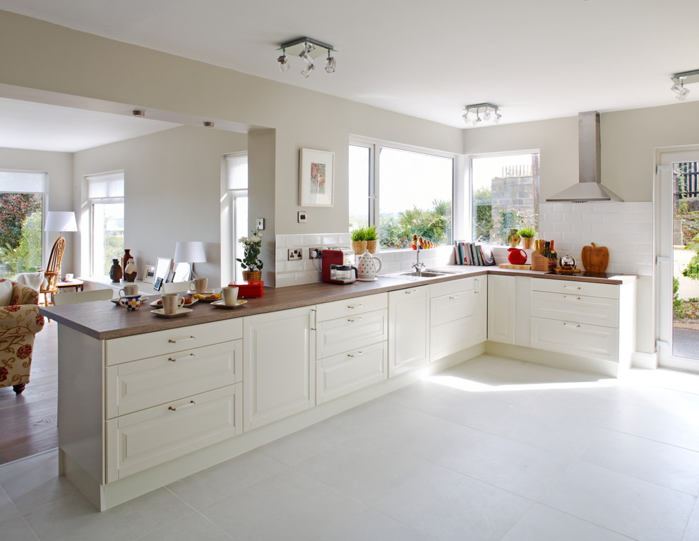 Photo of a transitional separate kitchen in Limerick with raised-panel cabinets, white cabinets, wood benchtops, white splashback, subway tile splashback and panelled appliances.