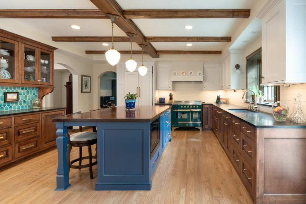 This is an example of a traditional u-shaped kitchen pantry in Kansas City with a single-bowl sink, recessed-panel cabinets, dark wood cabinets, quartz benchtops, white splashback, subway tile splashback, panelled appliances, light hardwood floors, with island and black benchtop.