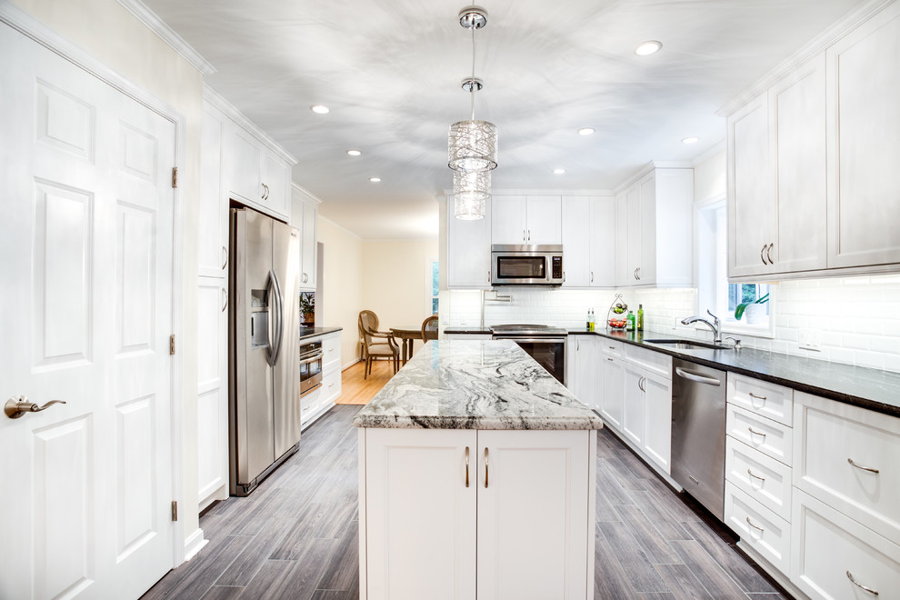 Photo of a large transitional u-shaped separate kitchen in Raleigh with recessed-panel cabinets, white cabinets, granite benchtops, white splashback, stainless steel appliances, with island, an undermount sink, subway tile splashback, medium hardwood floors and grey floor.