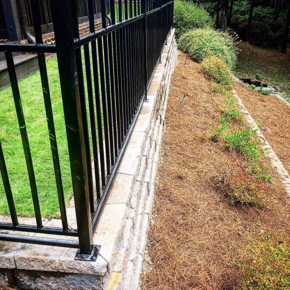 Traditional backyard garden in Birmingham with a retaining wall, concrete pavers and a metal fence.