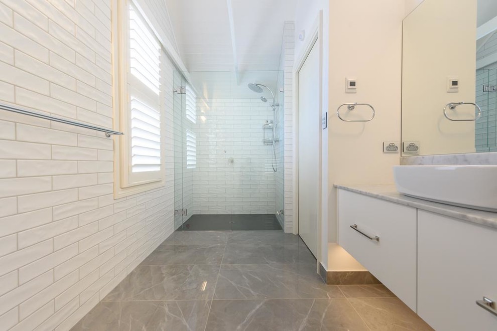 This is an example of a mid-sized traditional bathroom in Melbourne with flat-panel cabinets, white cabinets, an alcove shower, a two-piece toilet, white tile, ceramic tile, white walls, porcelain floors, a vessel sink, marble benchtops, grey floor and a hinged shower door.