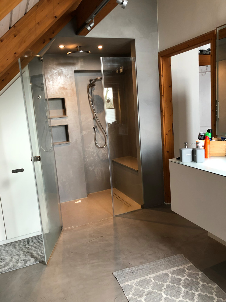 Mid-sized modern 3/4 bathroom in Cologne with flat-panel cabinets, grey cabinets, a curbless shower, a two-piece toilet, gray tile, stone slab, white walls, concrete floors, a drop-in sink, glass benchtops, grey floor, a hinged shower door, white benchtops, a shower seat, a single vanity, a built-in vanity, wood and brick walls.