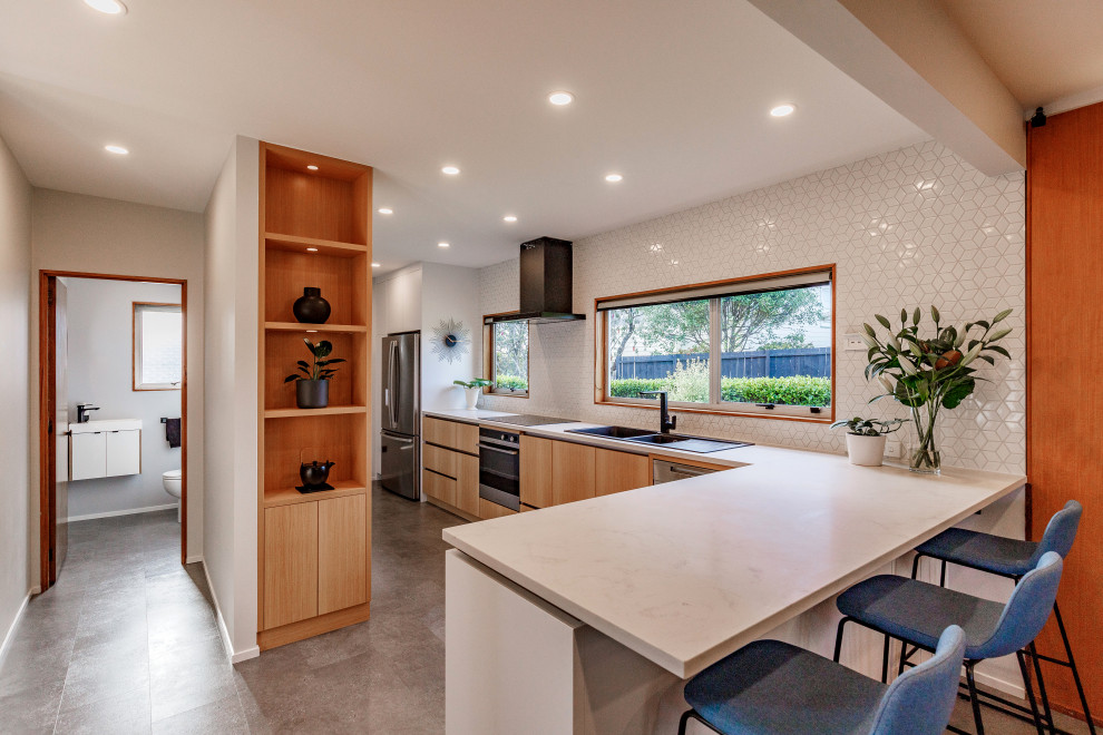 Photo of a mid-sized contemporary galley eat-in kitchen in Auckland with a double-bowl sink, quartz benchtops, white splashback, mosaic tile splashback, stainless steel appliances, linoleum floors, a peninsula, grey floor and white benchtop.