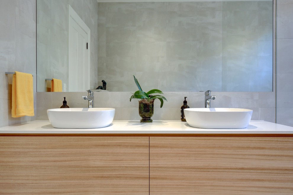 Photo of a mid-sized contemporary master wet room bathroom in Adelaide with furniture-like cabinets, light wood cabinets, a freestanding tub, a wall-mount toilet, gray tile, ceramic tile, ceramic floors, a console sink, engineered quartz benchtops, grey floor, an open shower and white benchtops.