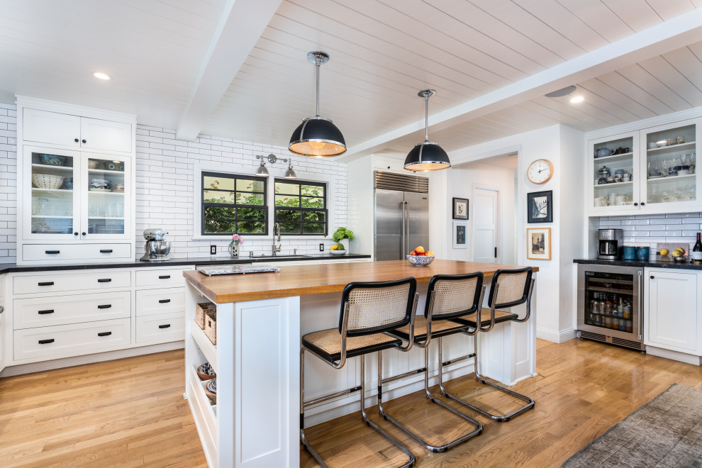 Mid-sized country u-shaped eat-in kitchen in Los Angeles with an undermount sink, shaker cabinets, white cabinets, wood benchtops, white splashback, subway tile splashback, stainless steel appliances, light hardwood floors, with island, brown floor, brown benchtop and timber.