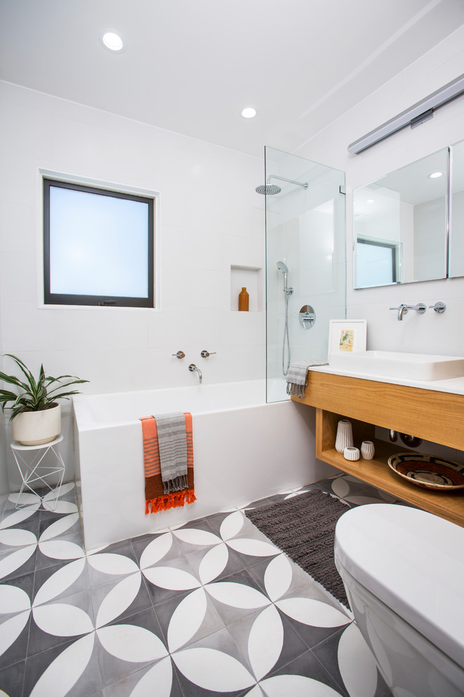 Mid-sized contemporary 3/4 bathroom in Los Angeles with open cabinets, medium wood cabinets, a corner tub, a shower/bathtub combo, white walls, a vessel sink, grey floor, a one-piece toilet, cement tiles, engineered quartz benchtops and an open shower.