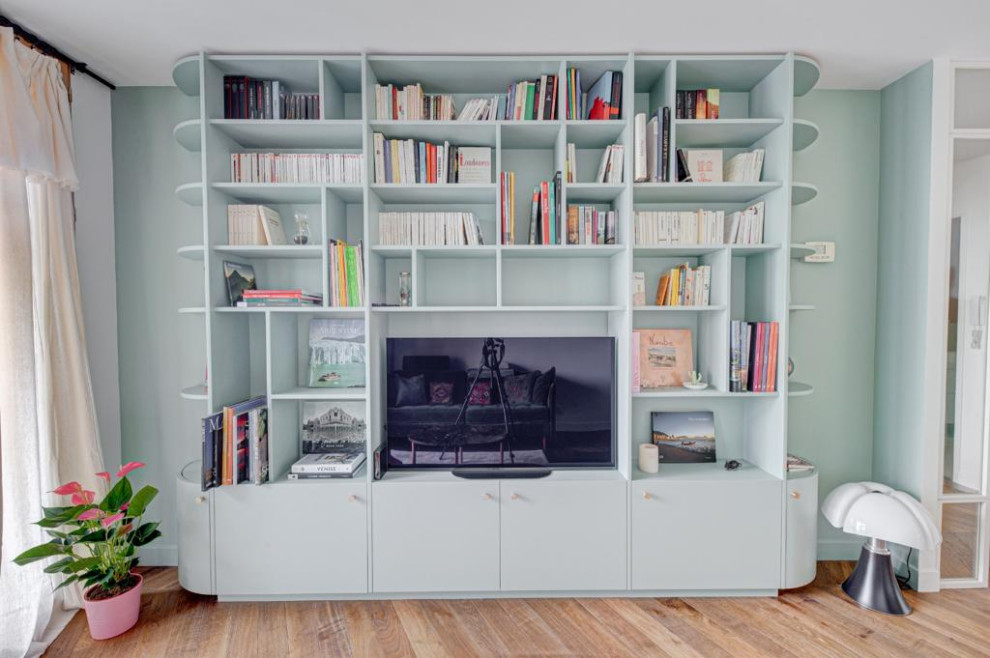 Diseño de sala de estar con biblioteca abierta minimalista pequeña sin chimenea con paredes verdes, suelo de madera clara, pared multimedia, suelo beige y vigas vistas