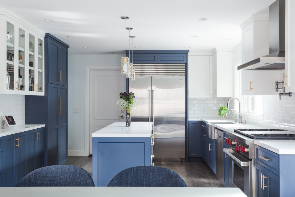 Photo of a transitional u-shaped kitchen in San Francisco with a farmhouse sink, shaker cabinets, blue cabinets, white splashback, stainless steel appliances, dark hardwood floors, with island, grey floor and white benchtop.
