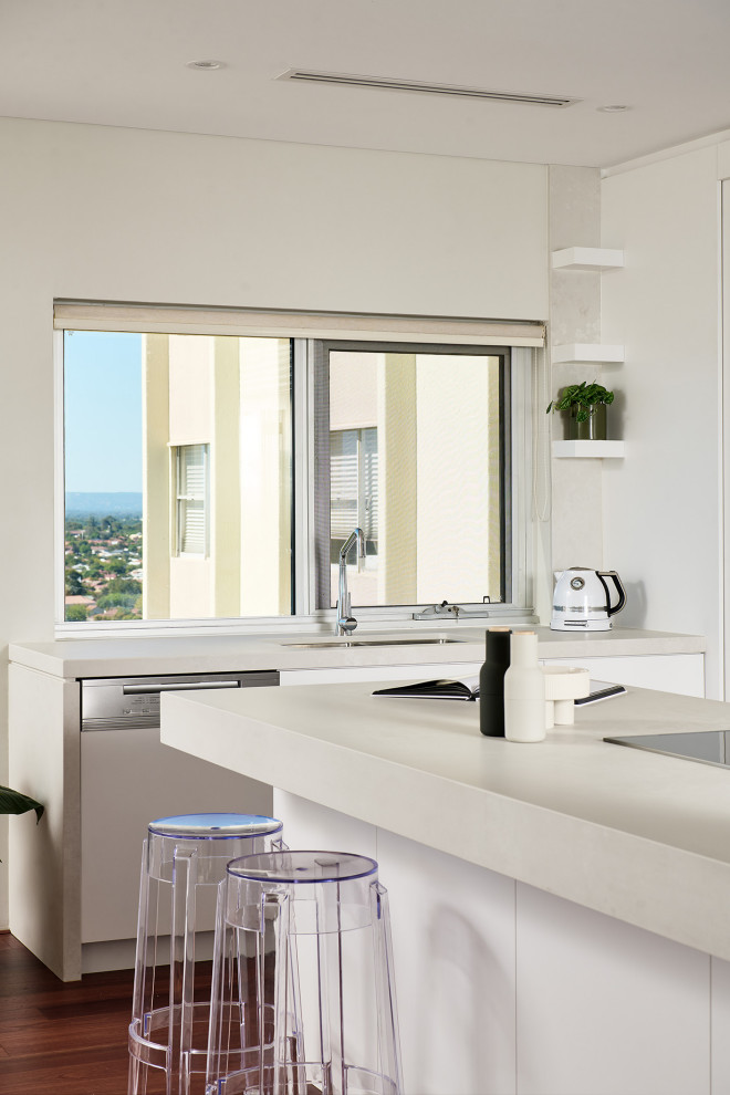 Inspiration for a mid-sized modern l-shaped open plan kitchen in Perth with an undermount sink, flat-panel cabinets, white cabinets, quartz benchtops, white splashback, ceramic splashback, black appliances, dark hardwood floors, with island, brown floor and white benchtop.