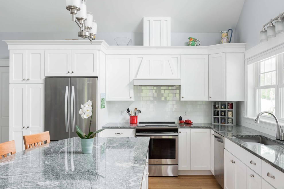 Photo of a large traditional l-shaped open plan kitchen in Portland Maine with a drop-in sink, shaker cabinets, white cabinets, granite benchtops, white splashback, subway tile splashback, stainless steel appliances, vinyl floors, with island and brown floor.