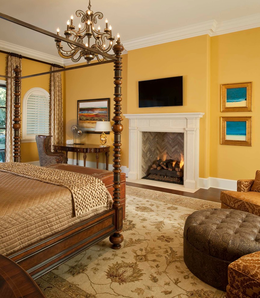 This is an example of a large mediterranean bedroom in Other with yellow walls, dark hardwood floors, a standard fireplace and brown floor.