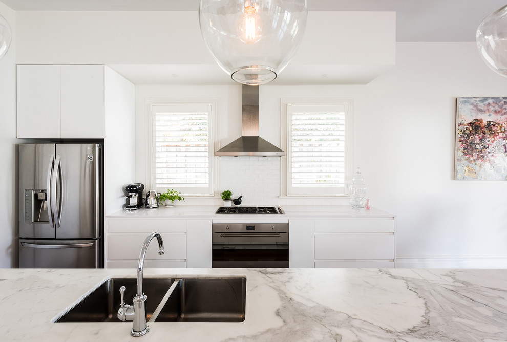 This is an example of a mid-sized contemporary single-wall open plan kitchen in Melbourne with an undermount sink, flat-panel cabinets, white cabinets, marble benchtops, white splashback, subway tile splashback, stainless steel appliances, dark hardwood floors, with island and brown floor.