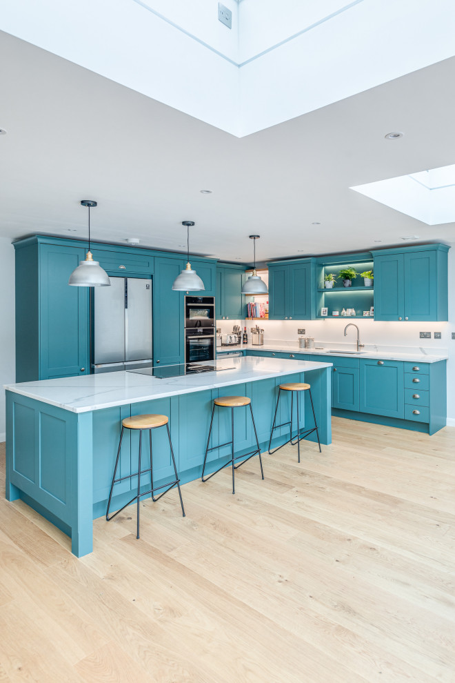 Inspiration for a large traditional l-shaped open plan kitchen in Hertfordshire with a drop-in sink, shaker cabinets, green cabinets, quartzite benchtops, panelled appliances, laminate floors, with island and white benchtop.