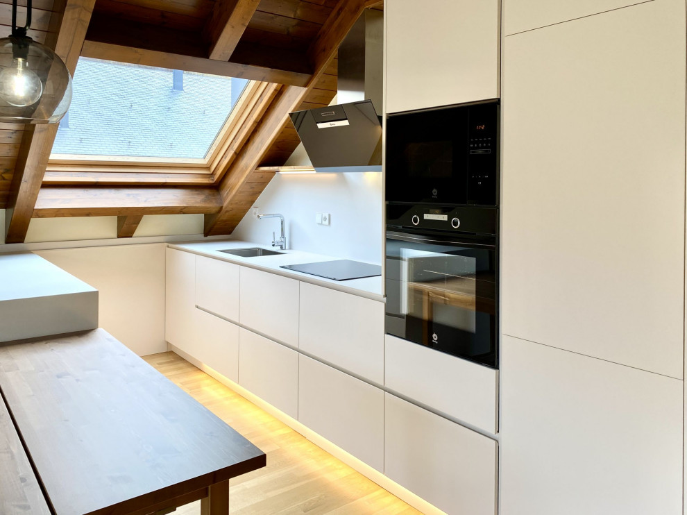 This is an example of a mid-sized country eat-in kitchen in Barcelona with an undermount sink, white cabinets, black appliances, light hardwood floors, with island, brown floor and wood.