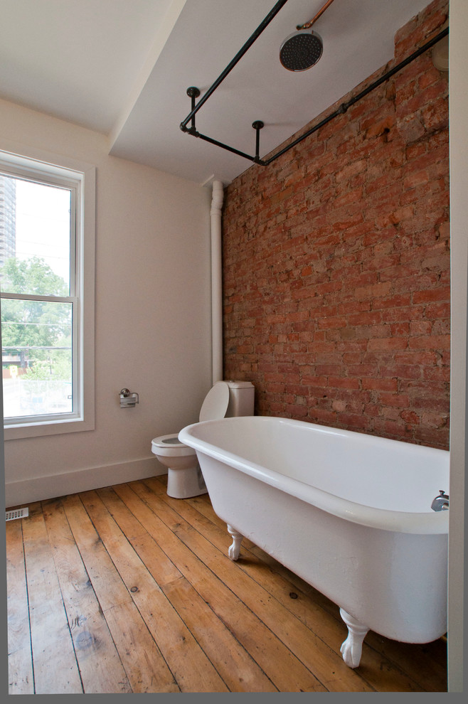 Cette photo montre une salle de bain industrielle de taille moyenne avec une baignoire sur pieds, un combiné douche/baignoire, un mur blanc et un sol en bois brun.