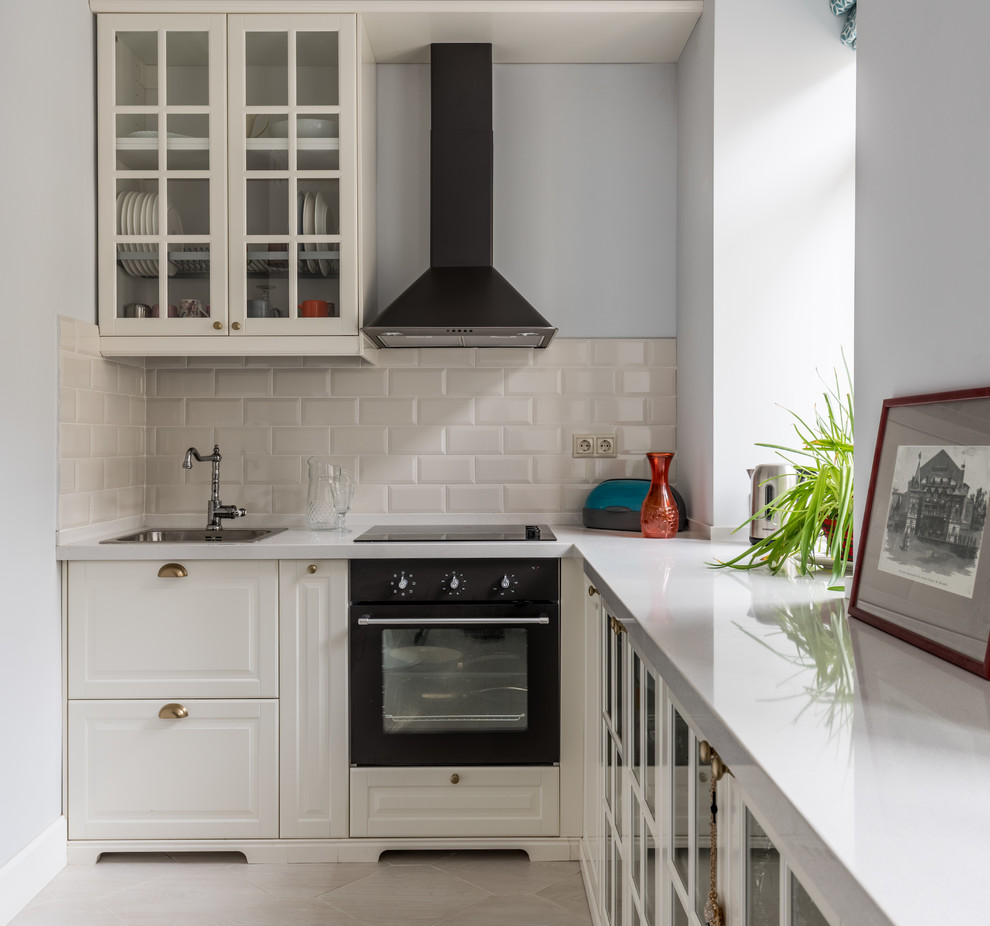 This is an example of a small transitional single-wall separate kitchen in Moscow with a drop-in sink, raised-panel cabinets, white cabinets, beige splashback, subway tile splashback, black appliances and no island.