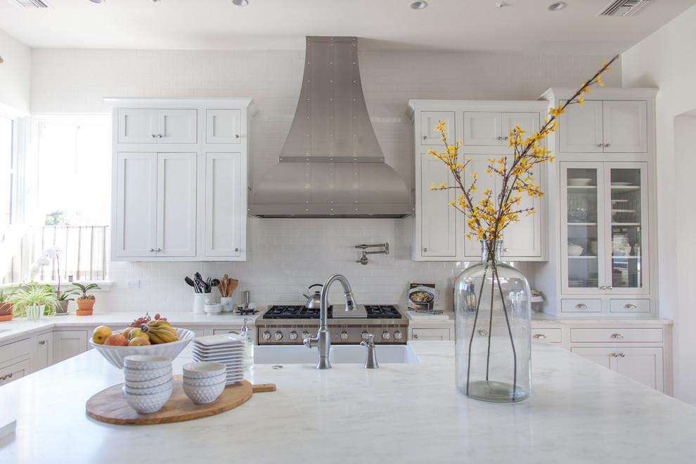Inspiration for a large transitional l-shaped light wood floor eat-in kitchen remodel in Phoenix with a farmhouse sink, white cabinets, white backsplash, stainless steel appliances, an island, shaker cabinets, stainless steel countertops and porcelain backsplash