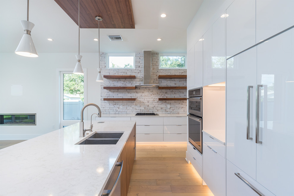 Design ideas for a mid-sized modern l-shaped open plan kitchen in Tampa with a double-bowl sink, flat-panel cabinets, white cabinets, quartz benchtops, beige splashback, ceramic splashback, stainless steel appliances, light hardwood floors, with island, beige floor and white benchtop.