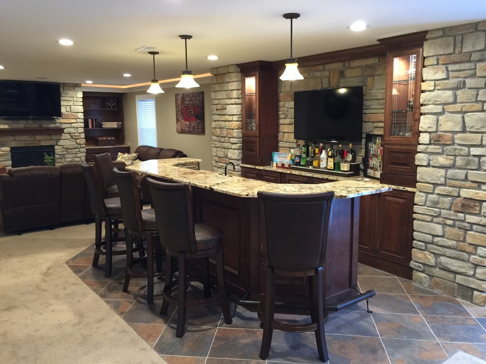 This is an example of a large arts and crafts seated home bar in St Louis with ceramic floors, raised-panel cabinets, granite benchtops, beige splashback, stone tile splashback, multi-coloured floor and dark wood cabinets.
