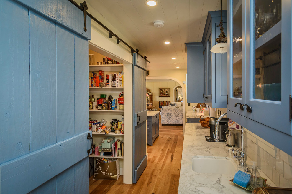 Mid-sized country l-shaped open plan kitchen in San Francisco with blue cabinets, marble benchtops, white splashback, subway tile splashback, medium hardwood floors, a farmhouse sink, shaker cabinets, stainless steel appliances, with island and brown floor.
