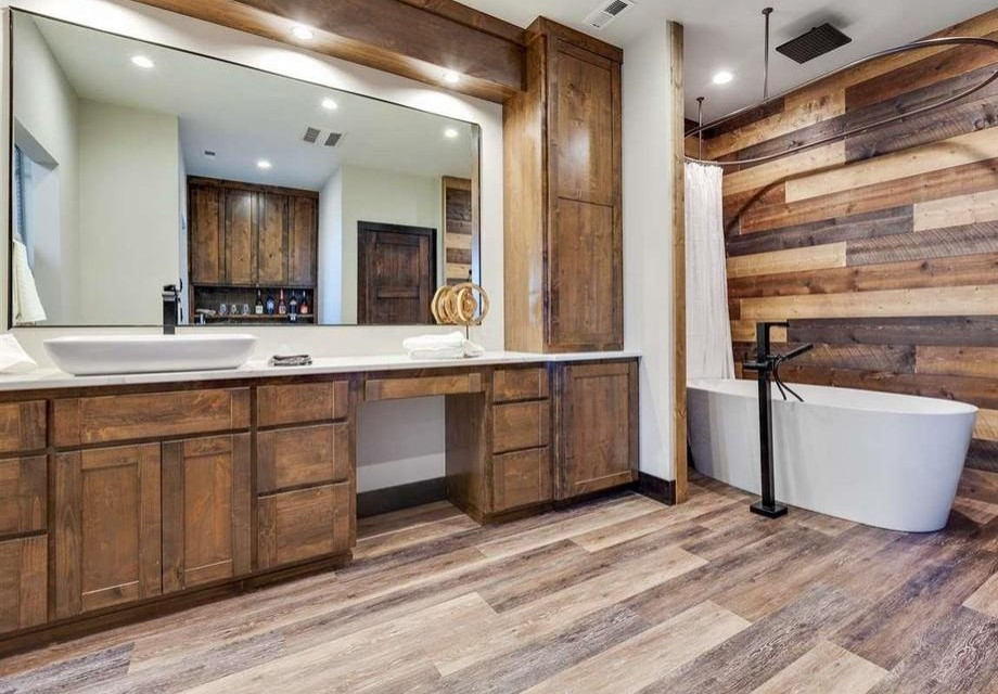 Design ideas for a mid-sized country master bathroom in Phoenix with open cabinets, medium wood cabinets, a freestanding tub, a shower/bathtub combo, a one-piece toilet, brown tile, wood-look tile, grey walls, medium hardwood floors, a trough sink, marble benchtops, brown floor, a shower curtain, white benchtops, an enclosed toilet, a single vanity, a built-in vanity and wood walls.