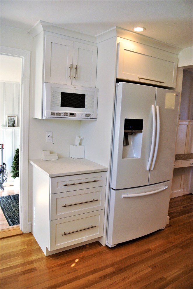 Example of a transitional u-shaped medium tone wood floor eat-in kitchen design in Boston with shaker cabinets, an undermount sink, white cabinets, white backsplash, white appliances and a peninsula