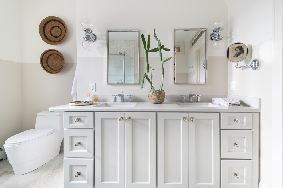 This is an example of a mid-sized transitional master bathroom in Philadelphia with recessed-panel cabinets, white cabinets, beige walls, an undermount sink, beige floor, a claw-foot tub, a corner shower, white tile, ceramic tile, solid surface benchtops, a hinged shower door and white benchtops.