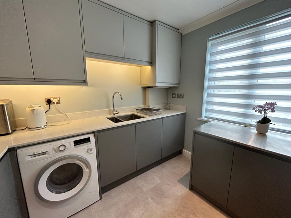 This is an example of a mid-sized u-shaped laundry cupboard in Dorset with a drop-in sink, flat-panel cabinets, quartzite benchtops, white splashback, engineered quartz splashback, grey walls, linoleum floors, grey floor and white benchtop.