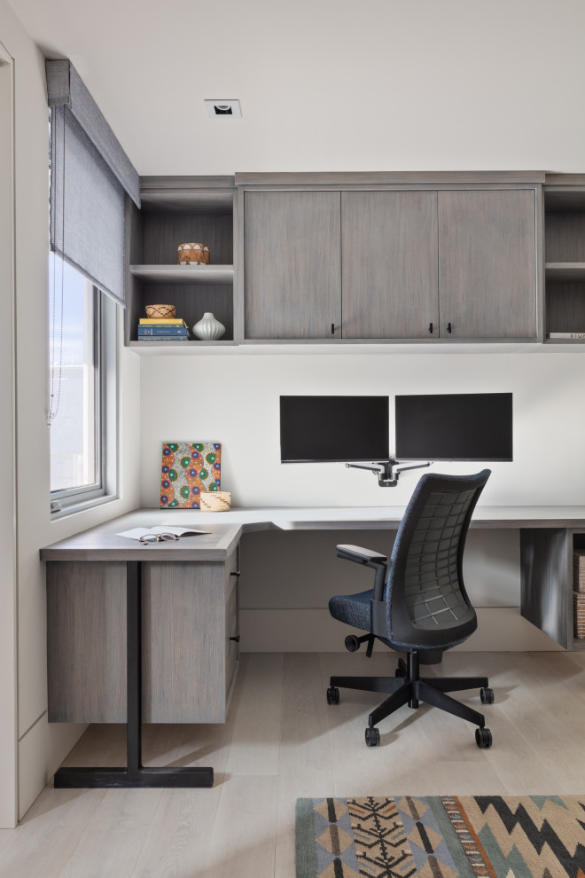 Photo of a contemporary home office in New York with white walls, light hardwood floors, a built-in desk and beige floor.