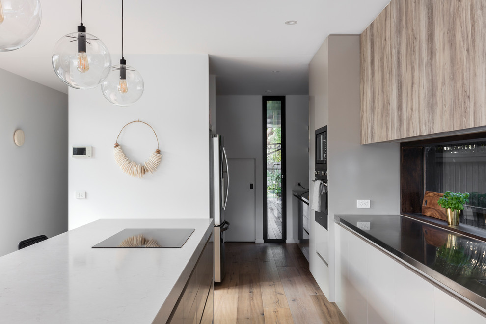 Design ideas for a mid-sized contemporary galley kitchen in Melbourne with a single-bowl sink, recessed-panel cabinets, medium wood cabinets, quartz benchtops, metallic splashback, mirror splashback, stainless steel appliances, light hardwood floors and with island.
