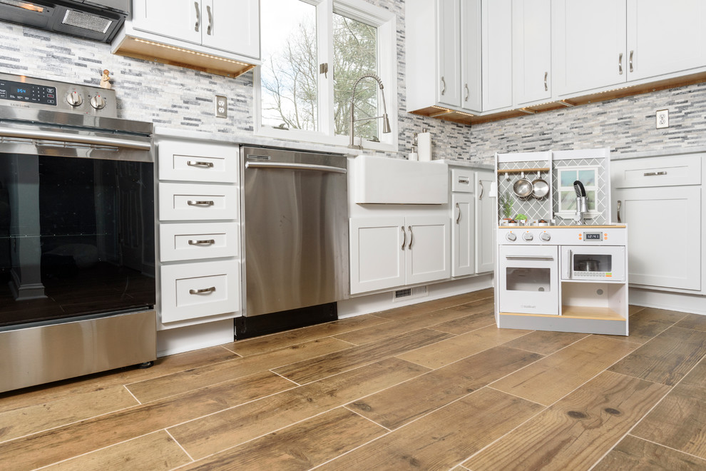 Inspiration for a large transitional l-shaped eat-in kitchen in Baltimore with a farmhouse sink, shaker cabinets, white cabinets, granite benchtops, grey splashback, stone tile splashback, stainless steel appliances, ceramic floors, no island, brown floor and white benchtop.