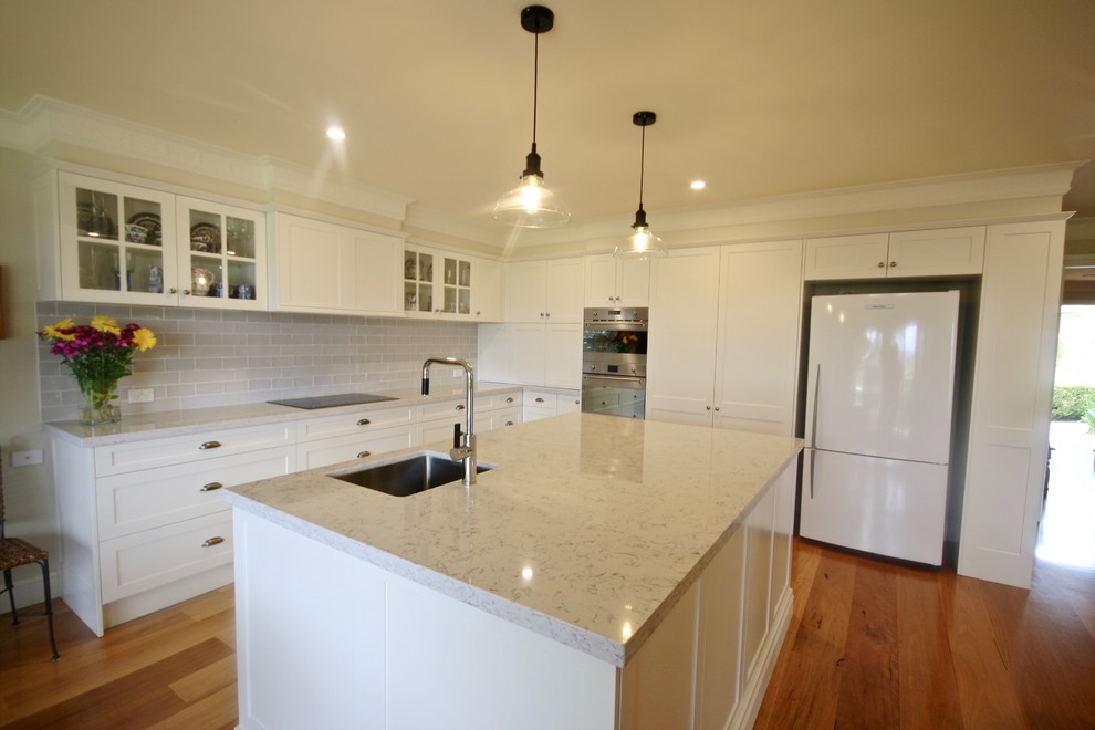 This is an example of a large transitional l-shaped eat-in kitchen in Sydney with an undermount sink, shaker cabinets, white cabinets, quartz benchtops, grey splashback, stone tile splashback, stainless steel appliances, medium hardwood floors and with island.