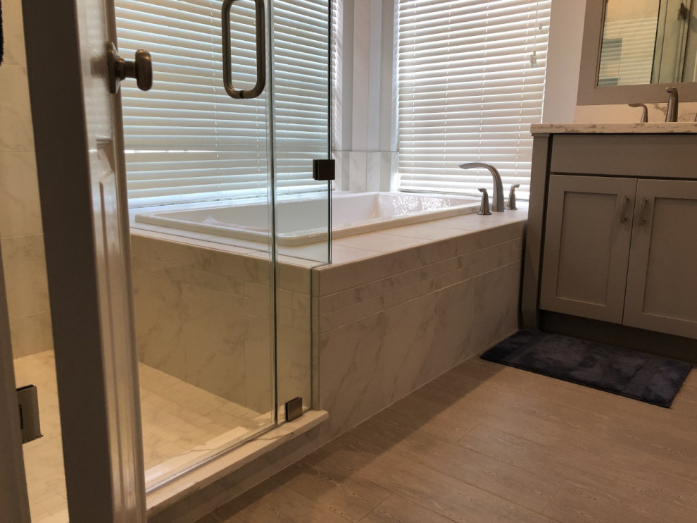 Example of a mid-sized transitional master white tile and porcelain tile porcelain tile and gray floor drop-in bathtub design in Houston with shaker cabinets, gray cabinets, a two-piece toilet, gray walls, an undermount sink, quartz countertops, a hinged shower door and white countertops