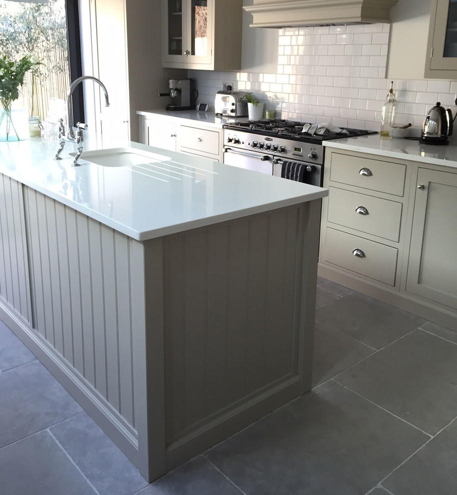Photo of a mid-sized traditional eat-in kitchen in Berkshire with shaker cabinets, green cabinets, white splashback, ceramic splashback, stainless steel appliances, limestone floors and with island.