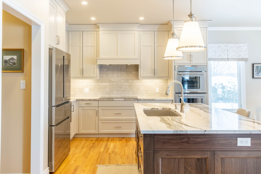 Design ideas for a mid-sized traditional l-shaped open plan kitchen in Ottawa with a single-bowl sink, recessed-panel cabinets, white cabinets, quartz benchtops, white splashback, porcelain splashback, stainless steel appliances, light hardwood floors, with island, beige floor and white benchtop.