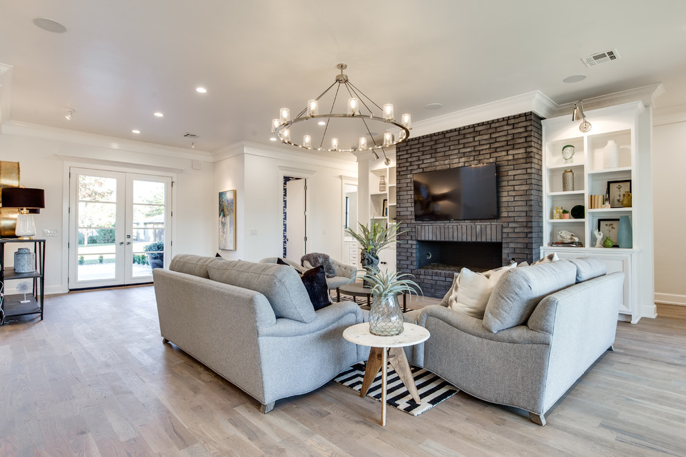 Photo of an expansive transitional formal open concept living room in Oklahoma City with white walls, medium hardwood floors, a standard fireplace, a brick fireplace surround and a wall-mounted tv.