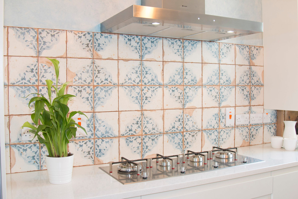 This is an example of a small eclectic l-shaped open plan kitchen with a built-in sink, flat-panel cabinets, beige cabinets, quartz worktops, beige splashback, cement tile splashback, stainless steel appliances, laminate floors, an island and brown floors.