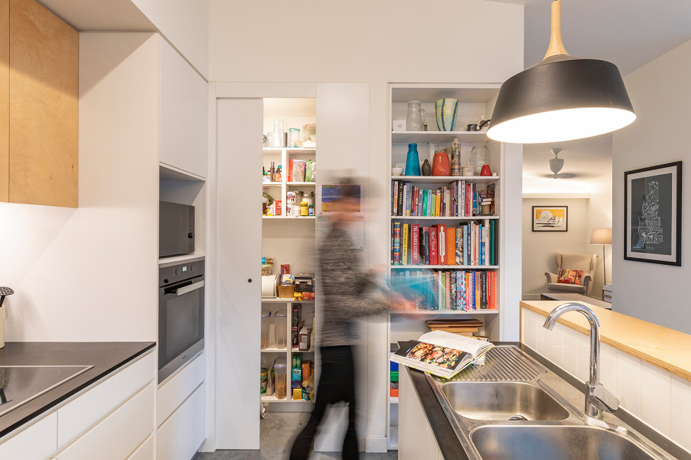 Small scandinavian galley open plan kitchen in Canberra - Queanbeyan with a drop-in sink, flat-panel cabinets, white cabinets, white splashback, ceramic splashback, stainless steel appliances, concrete floors, with island, grey floor and black benchtop.