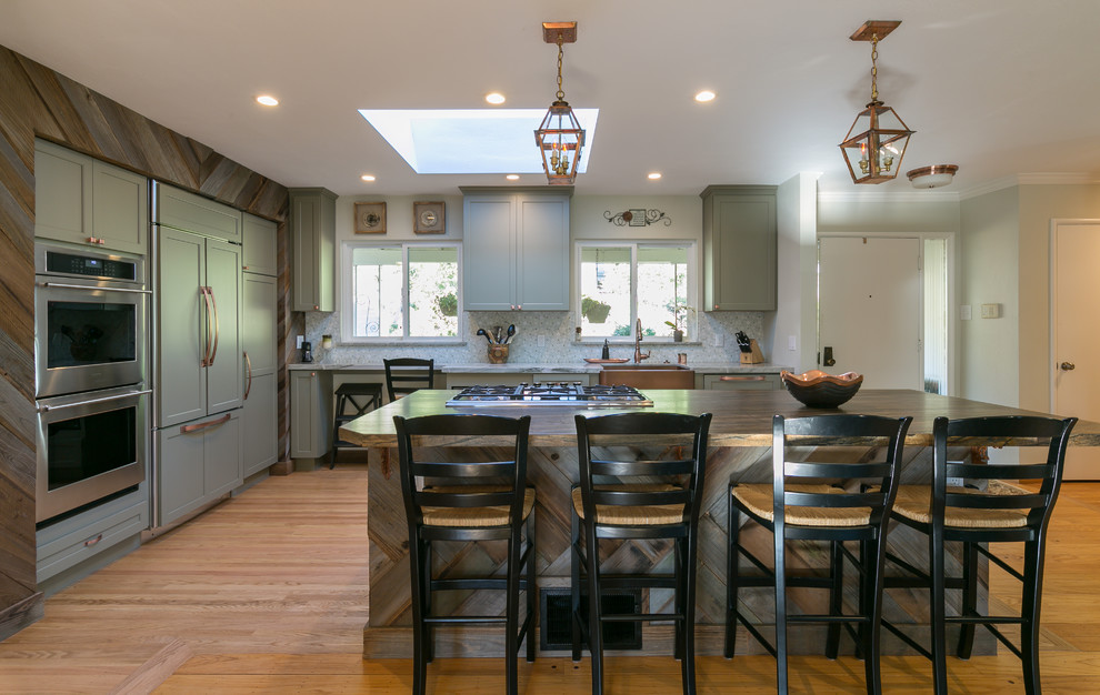 Open concept kitchen - large transitional l-shaped light wood floor open concept kitchen idea in San Francisco with a farmhouse sink, shaker cabinets, gray cabinets, multicolored backsplash, mosaic tile backsplash, paneled appliances, an island and granite countertops